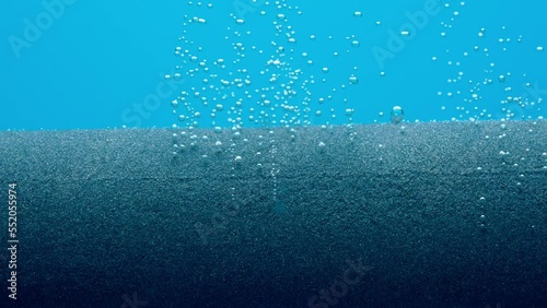 Small shiny air bubbles escaping from grey paralon compressor tube or filter under water. Macro shot of working equipment for aeration of water with oxygen in aquarium on blue background. Slow motion. photo