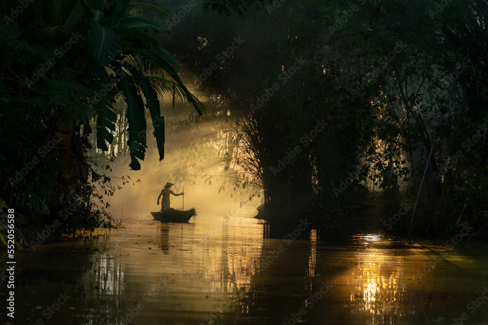 Φωτογραφία Photo of a local asian old man male boatman wearing conical hat rowing a small wooden boat across a small river during sunset time in a bamboo forest to deliver some dry grasses as animal feeds