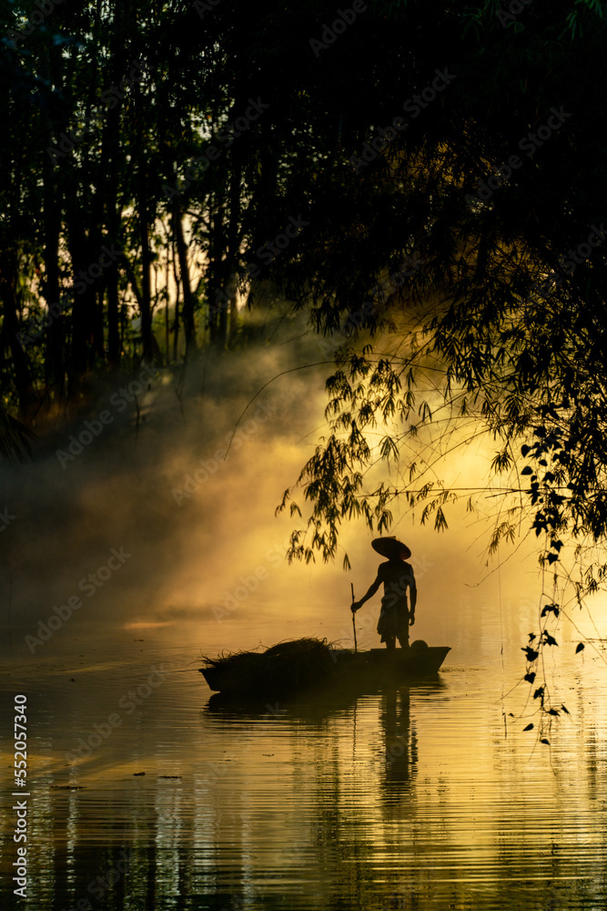 Φωτογραφία Photo of a local asian old man male boatman wearing conical hat rowing a small wooden boat across a small river during sunset time in a bamboo forest to deliver some dry grasses as animal feeds