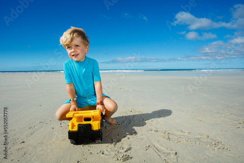 Boy play with and sit on truck toy at the sand sea beach