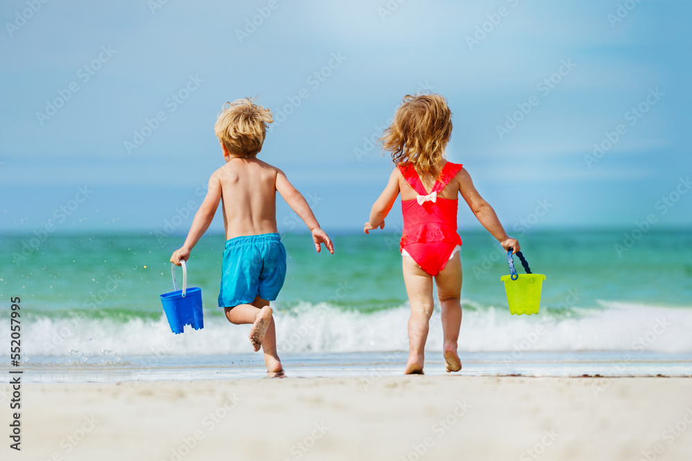 View from behind of a boy and girl run with bucket to ocean View from behind of a boy and girl run with bucket to ocean