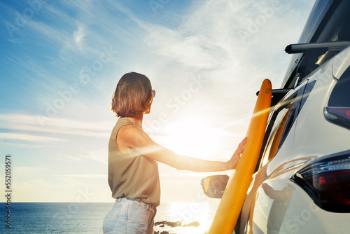 Canvas Print Woman stand with surf board by the car looking over ocean sunset
