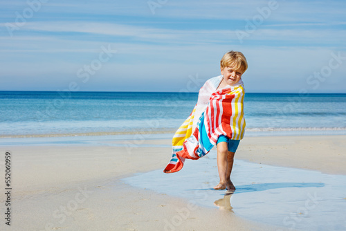 Happy boy in towel run after swim on sea sand beach