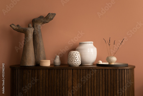 Tableau sur toile Interior design of harmonized living room interior with wooden commode, modern hands sculpture, vase with dried flowers, beige casket, pink wall and personal accessories