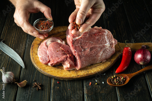 The cook sprinkles raw meat with dry spices. Preparing beef meat before roasting. Working environment in the kitchen of a restaurant or cafe
