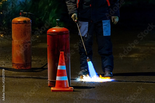 The flame of a gas burner in a selective focus during patching the road to heat up the asphalt pavement, preparing the road for a layer of bitumen. photo