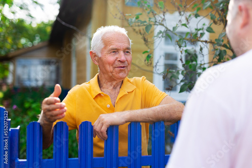 Elderly man discussing with neighbour beside house photo