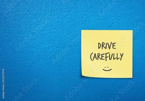 Bright blue wall copy space background with yellow note written with smiley DRIVE CAREFULLY , remind car driver or bike rider to drive carefully with awareness of safety first on the road