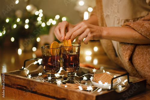 Female hands hold cup of tea next to cookies and Christmas tree on tray. Selective focus.