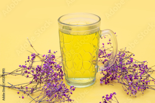 Uma caneca de vidro com chá com pequenos galhos de flores em um fundo amarelo. Formato horizontal. photo