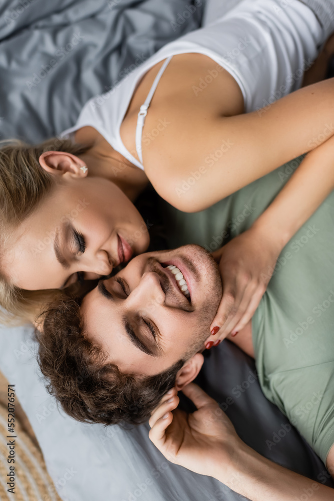 Top view of young woman in pajama touching neck of positive boyfriend on bed. Top view of young woman in pajama touching neck of positive boyfriend on bed.