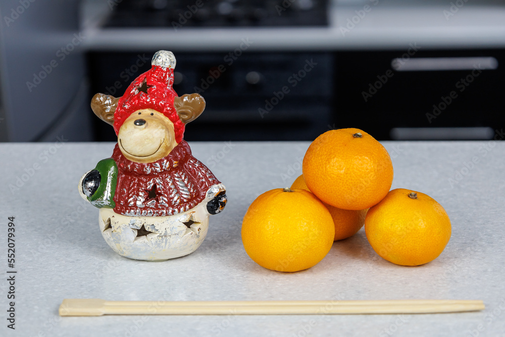 Three Mandarins and chopsticks and a Christmas figurine on a white table against a dark kitchen background