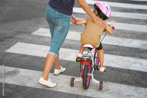 Mother goes pedestrian crossing with daughter on bicycle. Woman with child crossing the road in the city 