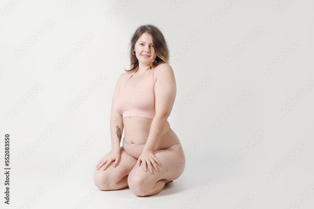 Obraz premium A plump woman with a hairstyle, smiling at the camera, sitting in the studio in her underwear. A bodypositive large-sized woman who feels comfortable in her natural body.