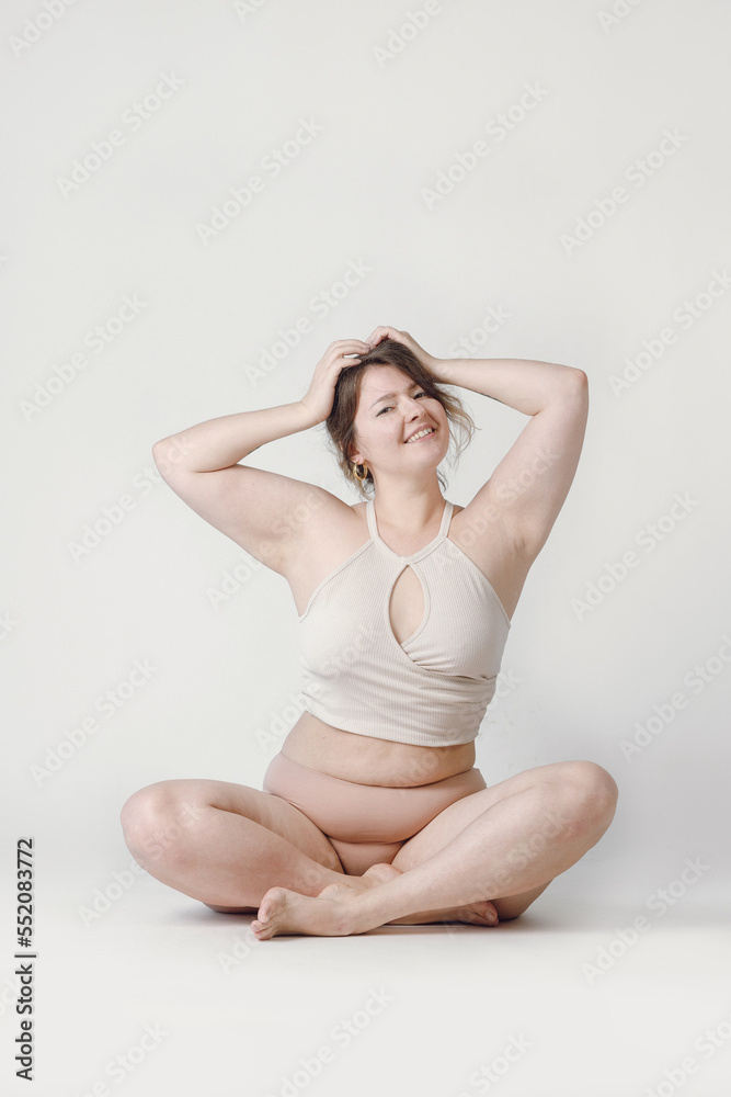 Fototapeta premium A plump woman with a hairstyle, smiling at the camera, sitting in the studio in her underwear. A bodypositive large-sized woman who feels comfortable in her natural body.