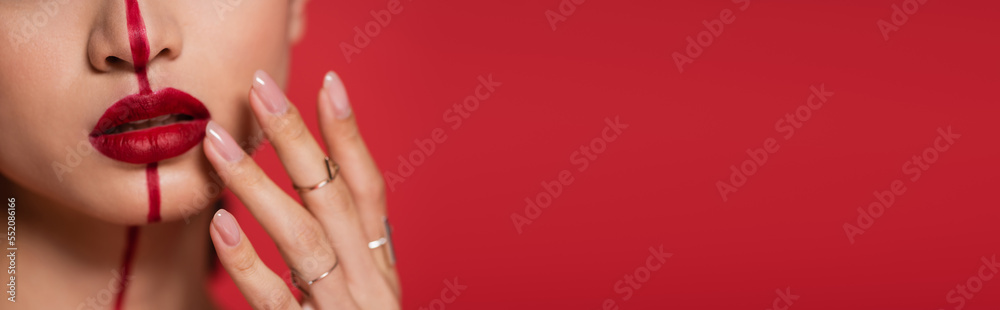 Naklejka premium cropped view of woman with makeup touching bright lips isolated on red, banner.