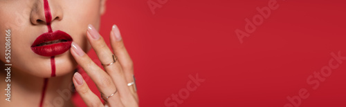cropped view of woman with makeup touching bright lips isolated on red  banner.