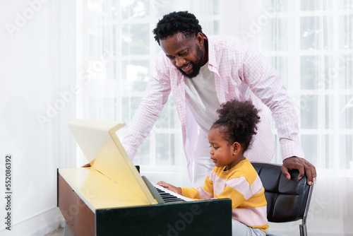 A father is teaching his young daughter to play the piano or the electone in the living room of the house. photo