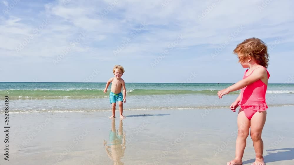 Boy and sister girl run on the sand beach smiling over sea waves Boy and sister girl run on the sand beach smiling over sea waves