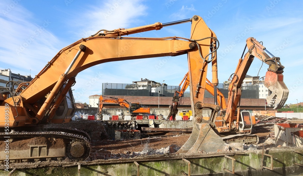 Group of heavy excavators at work in the ruins of a demolished building for an urban redevelopment Group of heavy excavators at work in the ruins of a demolished building for an urban redevelopment