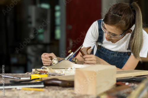 Young Asian carpenter woman working with wood in carpentry woodworking workshop, Capenter Concept