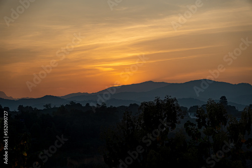 orangener goldener Sonnenuntergang in Chiang Rai, Norden von Thailand mit Bergen im Hintergrund, hinter welche die Sonne verschwindet