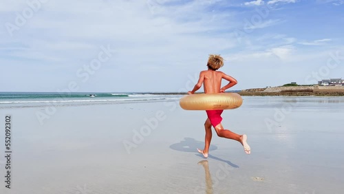 Handsome boy with inflatable doughnut buoy run on the sand beach