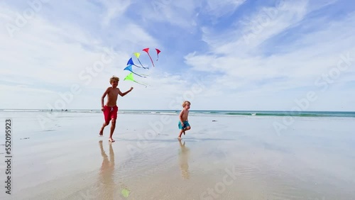 Boys brothers run together holding colorful kites set at beach
