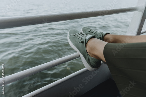 Detail of womans legs in green sneakers and green skirt resting on the railing of the ferry © Tomáš Hudolin