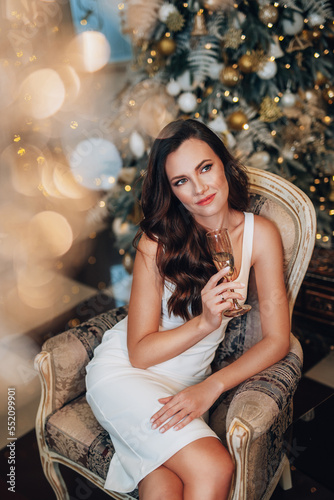 Stylish beautiful woman in a New Year's dress sits in a chic restaurant. A young slender girl in an evening dress stands in a New Year's studio. Happy girl celebrates christmas and drinks champagne. © Ольга Боровских