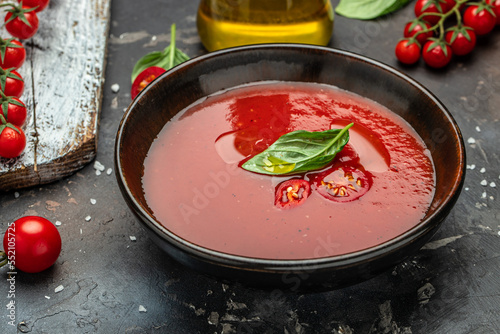Tomato soup with basil in a bowl on a dark background. top view