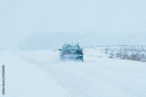 The car is driving on a road in a blizzard