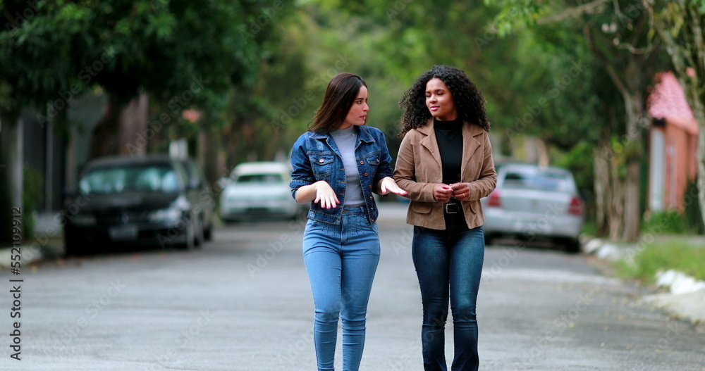 Two women walking together in conversation. Diverse girlfriends speaking in street walk