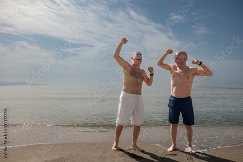 coppia di anziani amici al mare esulta portando i pugni al cielo 