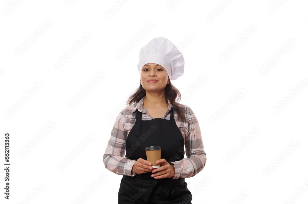 Isolated portrait on white background, of a charming positive woman barista waitress, wearing chef's hat and black apron, posing with takeaway coffee in recyclable cardboard cup, looking at camera Isolated portrait on white background, of a charming positive woman barista waitress, wearing chef's hat and black apron, posing with takeaway coffee in recyclable cardboard cup, looking at camera