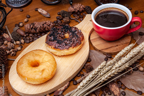 Pączki z dziurką (donaty) na drewnianej desce do krojenia i czarna kawa w filiżance na drewnianej podstawce