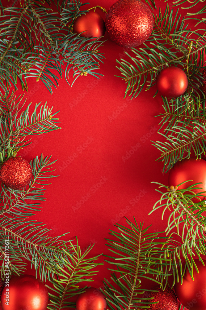 Nature frame Christmas background design with copy space. Happy New Year. Pine tree branches and and red decorative balls on a red color background. Flat lay arrangement.