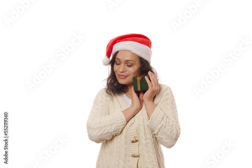 Multi-ethnic brunette wearing Santa hat and beige knitted sweater  hugging her happy present for Christmas or New Year. Boxing Day. Xmas - December 25th. Happy atmosphere of upcoming winter holidays