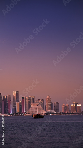Traditional boat sail in Corniche area with amazing sunset view of cityscape skyscraper buildings in Doha, Qatar, vertical shot
