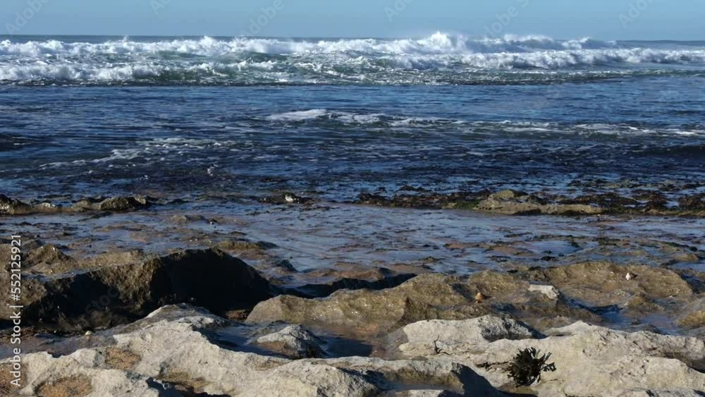 A powerful ocean wave crashes and breaks, creating foamy white spray as it approaches a rocky shoreline. A powerful ocean wave crashes and breaks, creating foamy white spray as it approaches a rocky shoreline.