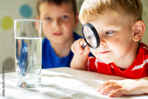 The child boy looking at water in a glass through magnifying glass photo