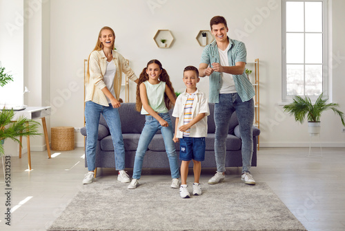 Spending active free time at home. Happy family of four is having fun dancing to music in living room of bright apartment. Excited young married couple dancing with playful little children.