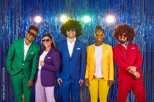 Men and women happy laughing people in sunglasses and colourful suits in gangnam style on blue shiny background with lights. Group of friends in funny curly wigs having fun at night club disco party