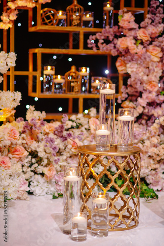Event decoration with golden stand and lighting candles among floral compositions