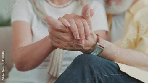 Close up view of a hands senior couple holding hands while resting on a couch. Hugging sitting at home. Tenderness. Beautiful family. Husband and wife
