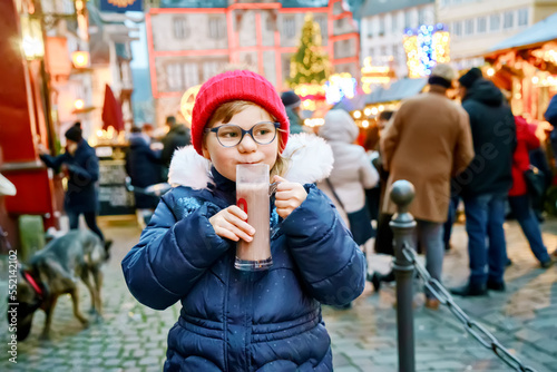 Little cute preschool girl drinking hot children punch or chocolate on German Christmas market. Happy child on traditional family market in Germany, Laughing boy in colorful winter clothes