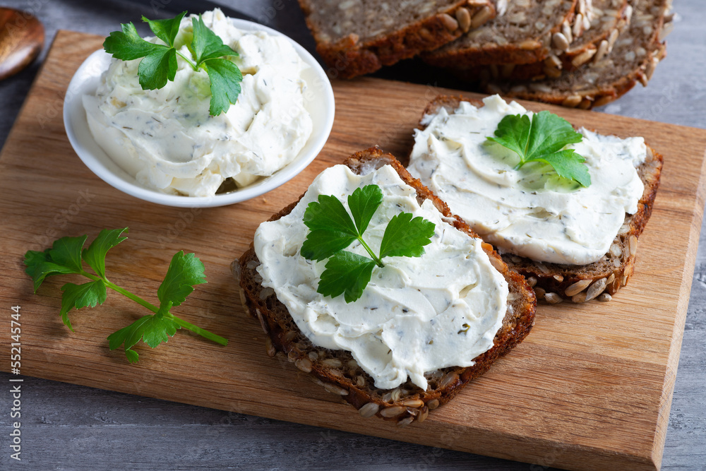 Home made bread on a wooden cutting board with curd cheese and ricotta and herbs. Decorated with green herbs Home made bread on a wooden cutting board with curd cheese and ricotta and herbs. Decorated with green herbs
