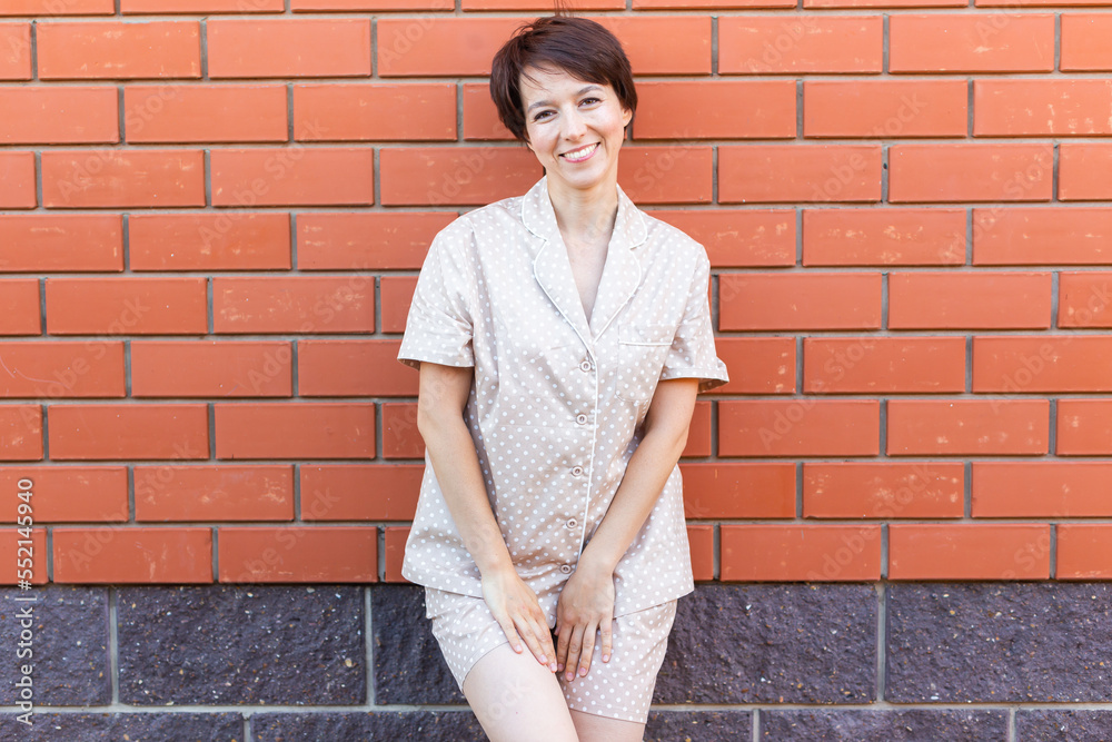 Cheerful woman in home wear pajama outdoor brick wall background emotions copy space and empty place for text - sleepwear and homewear concept Cheerful woman in home wear pajama outdoor brick wall background emotions copy space and empty place for text - sleepwear and homewear concept