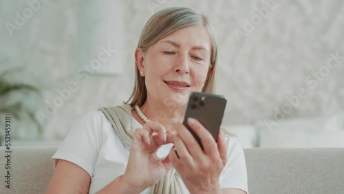 Close up portrait smiling elder middle age woman using smartphone sitting on sofa at home in modern apartment. Communication. Mobile. Internet. Cellphone message