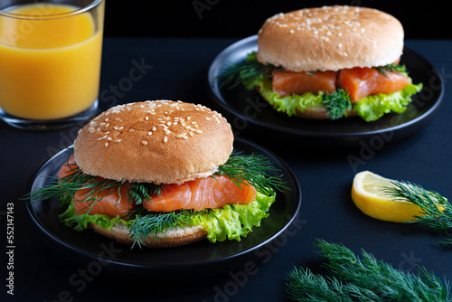 Healthy burger with salted salmon and orange juice on dark background